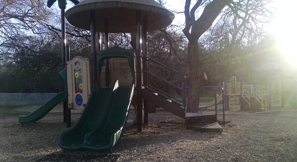 Playscape at dawn with sun coming up behind the trees. A slide is in the foreground.