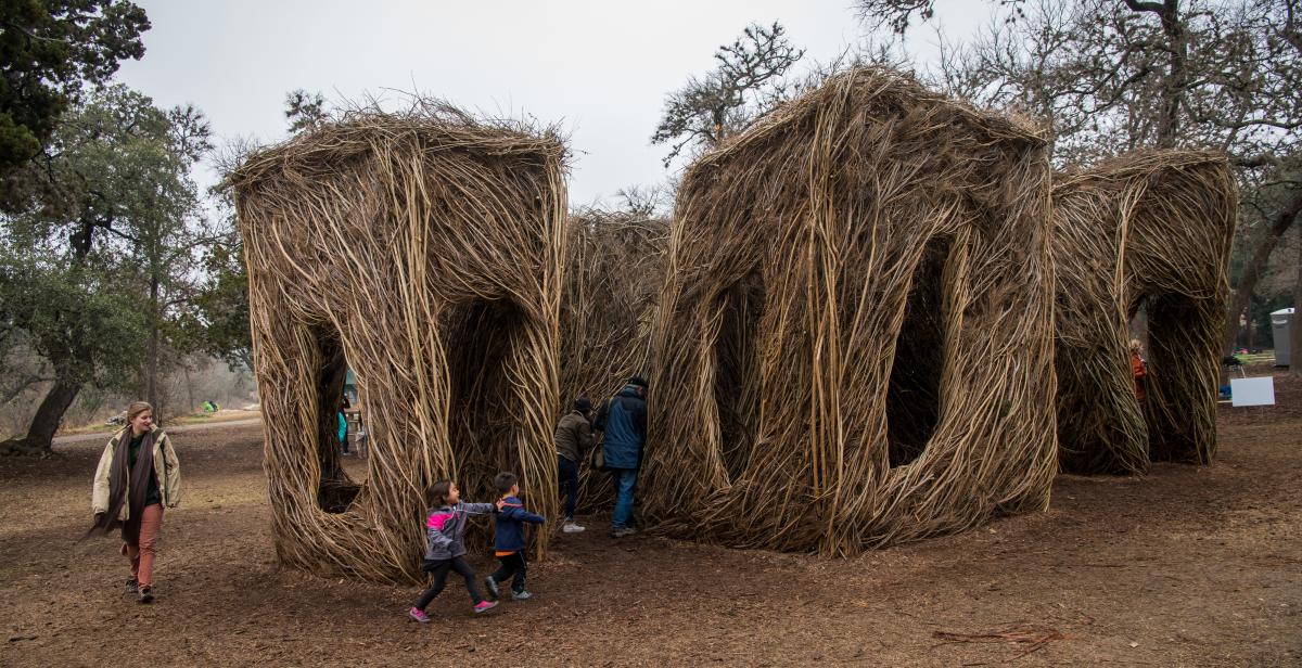 Artwork made of large sticks that children are runnign around and playing inside of.